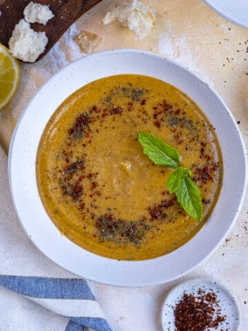 Turkish lentil soup garnished with fresh mint and spices in a white bowl.