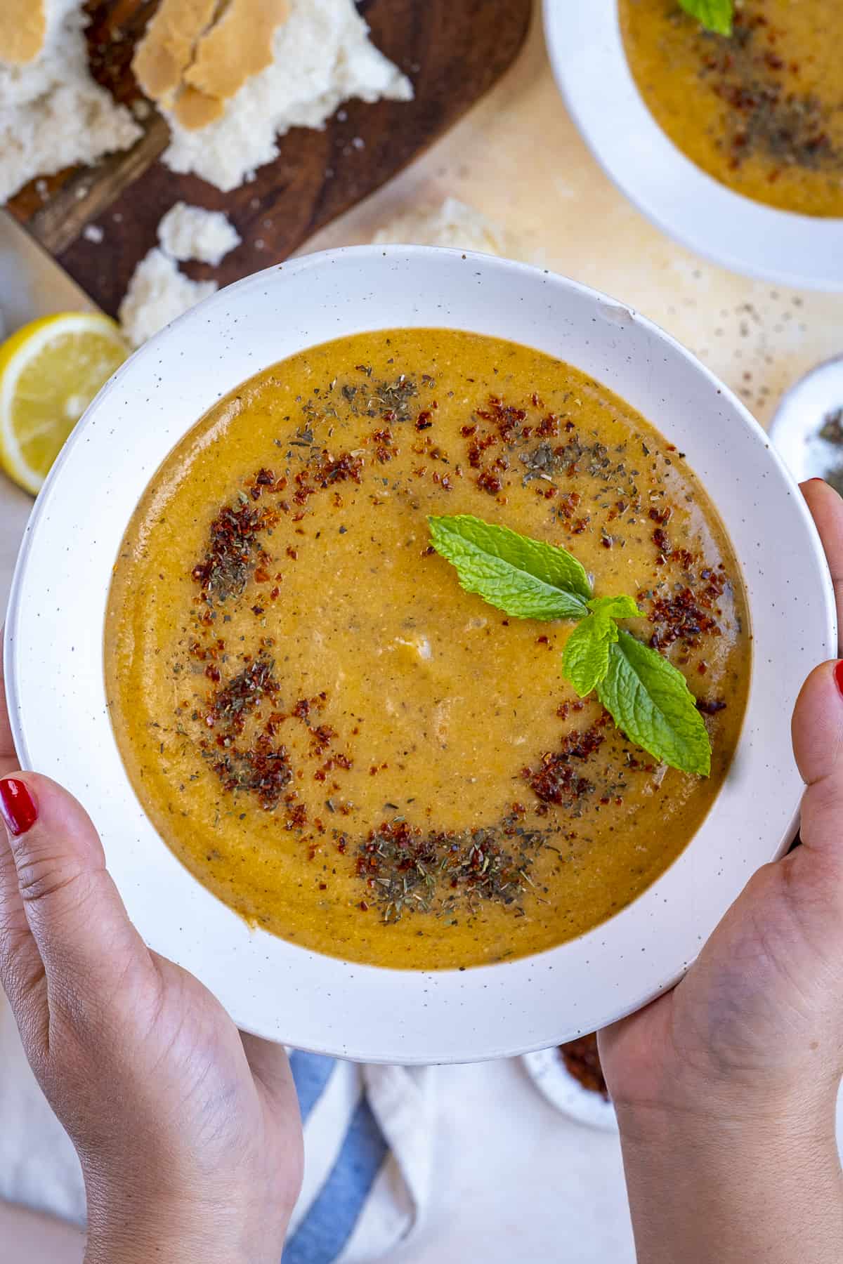 Woman holding a bowl of lentil soup garnished with fresh mint and spices.