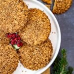 Turkish tahini sesame cookies on a white plate, holly berries in the middle and pine branch on the side.