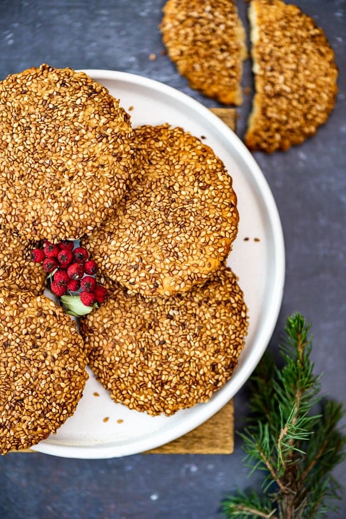 Turkish tahini sesame cookies on a white plate, holly berries in the middle and pine branch on the side.