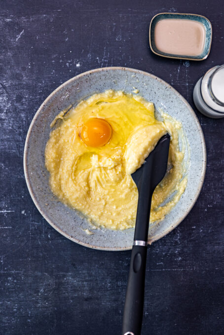 Butter, olive oil, powdered sugar and an egg in a ceramic bowl, a black spatula in it.