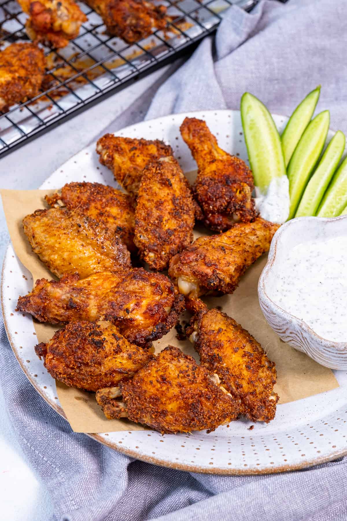 Chicken wings served with a ranch sauce and cucumber sticks on a white plate.
