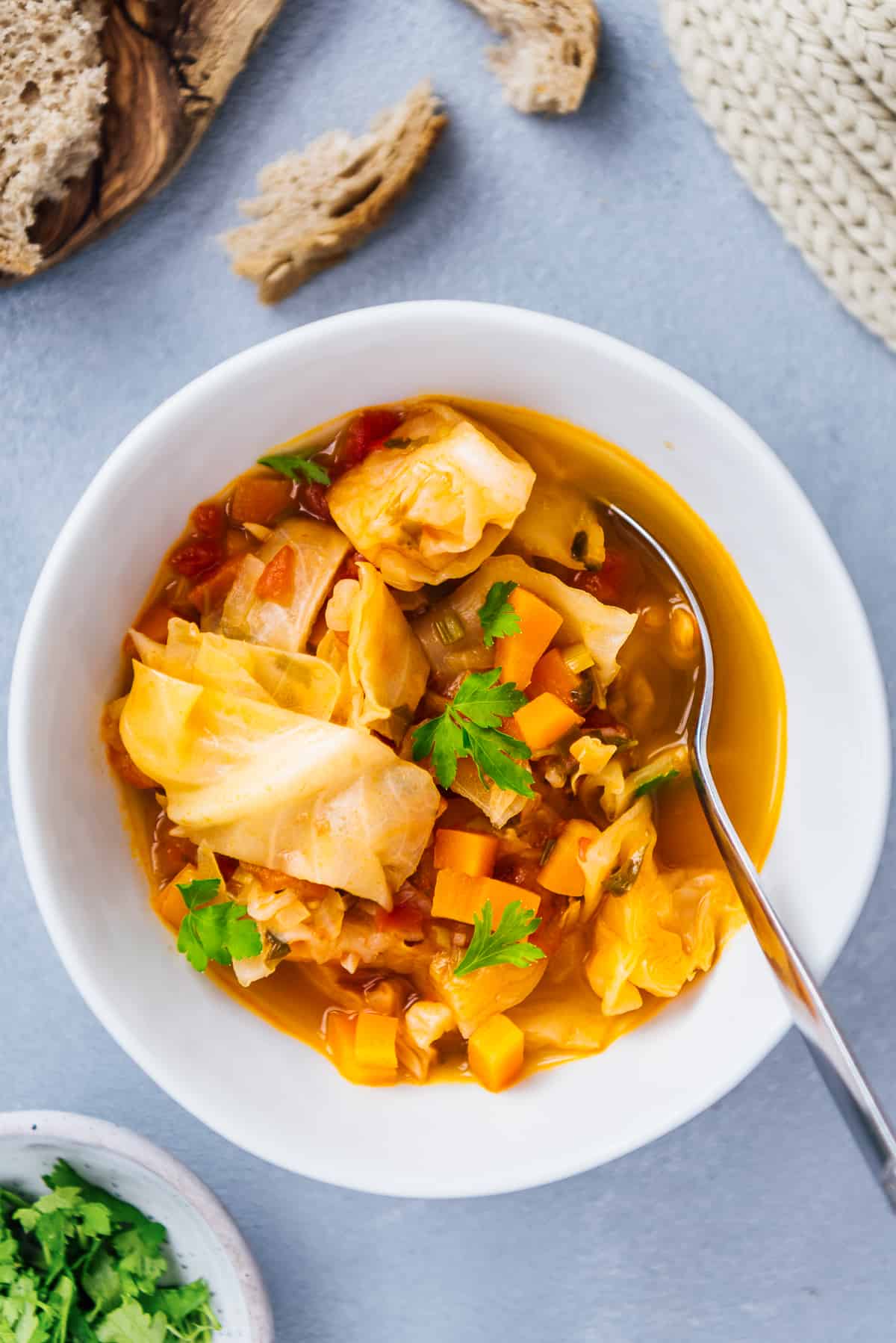 Cabbage soup served in a white bowl, bread slices, parsley on the side.