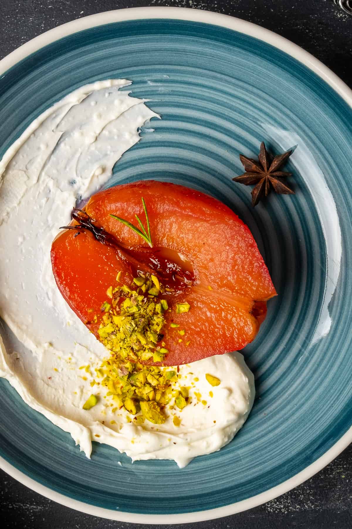 Cooked quince dessert served with clotted cream, garnished with pistachios on a blue plate.