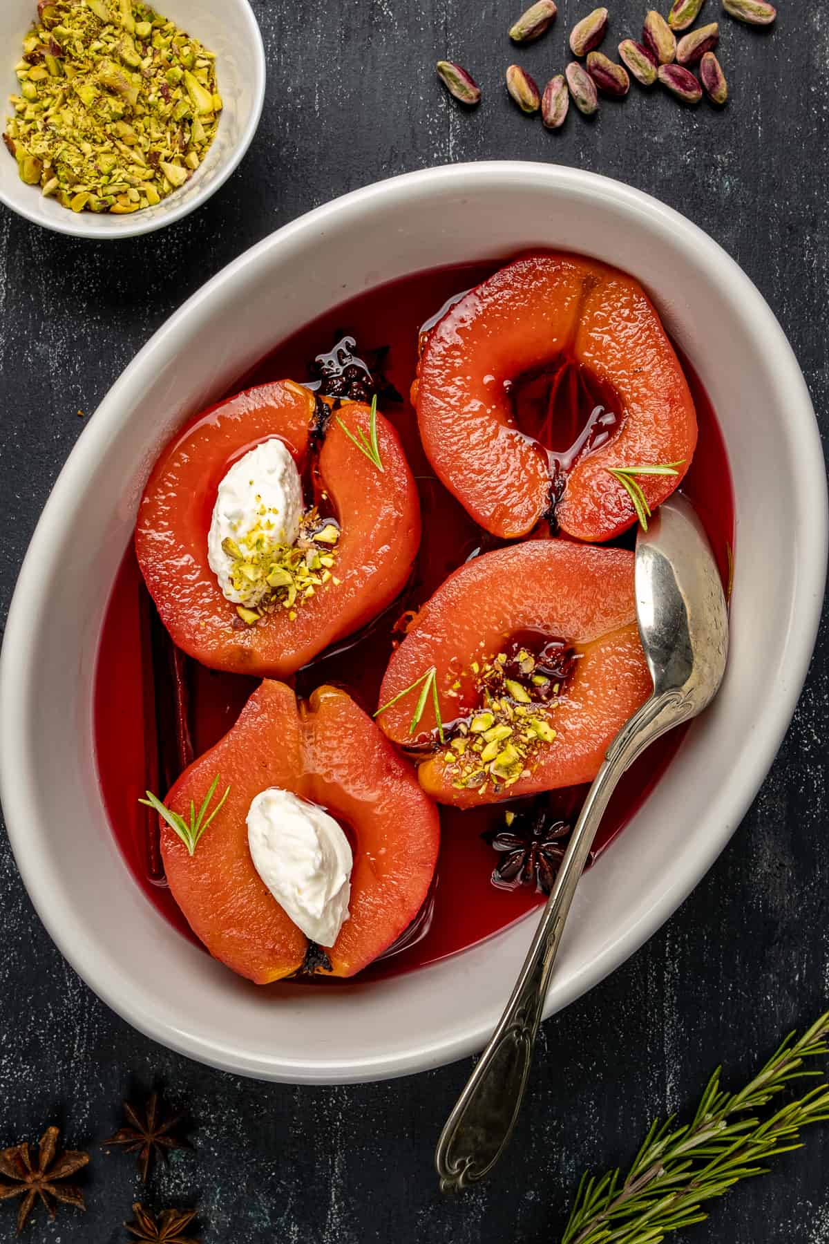 Turkish quince dessert garnished with clotted cream and ground pistachio in a white oval bowl and a spoon inside it.