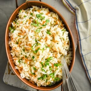 Rice with orzo served in an oval pan and two spoons inside it.