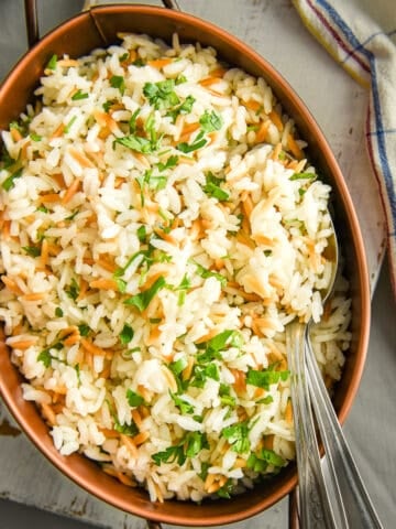 Rice with orzo served in an oval pan and two spoons inside it.