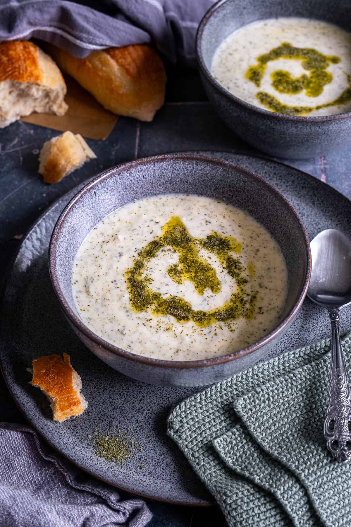 Two bowls of Turkish Yogurt Soup (Yayla Çorbası) topped with butter-mint sauce, served with bread and a spoon on the side.