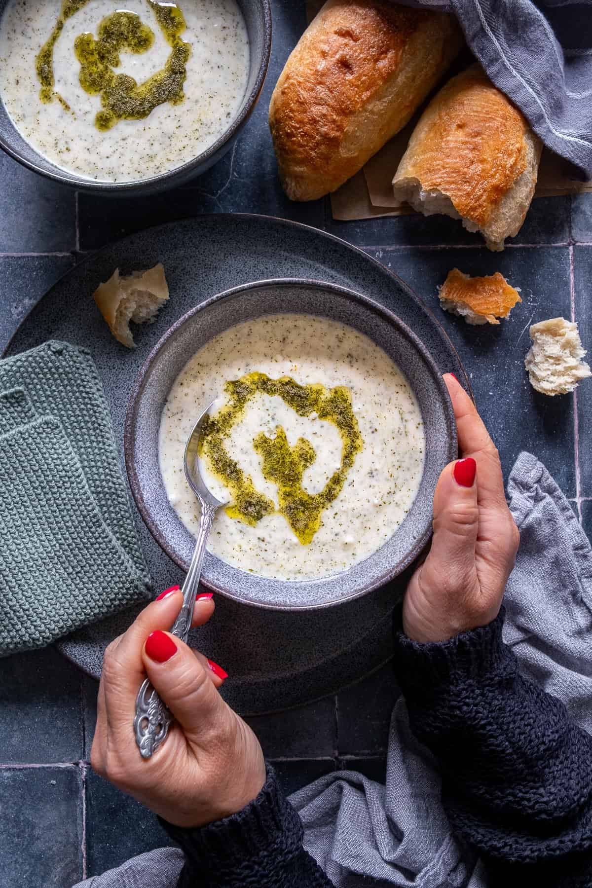 A person holding a bowl of Turkish Yogurt Soup (Yayla Çorbası) with butter-mint sauce on top, served with crusty bread on the side.