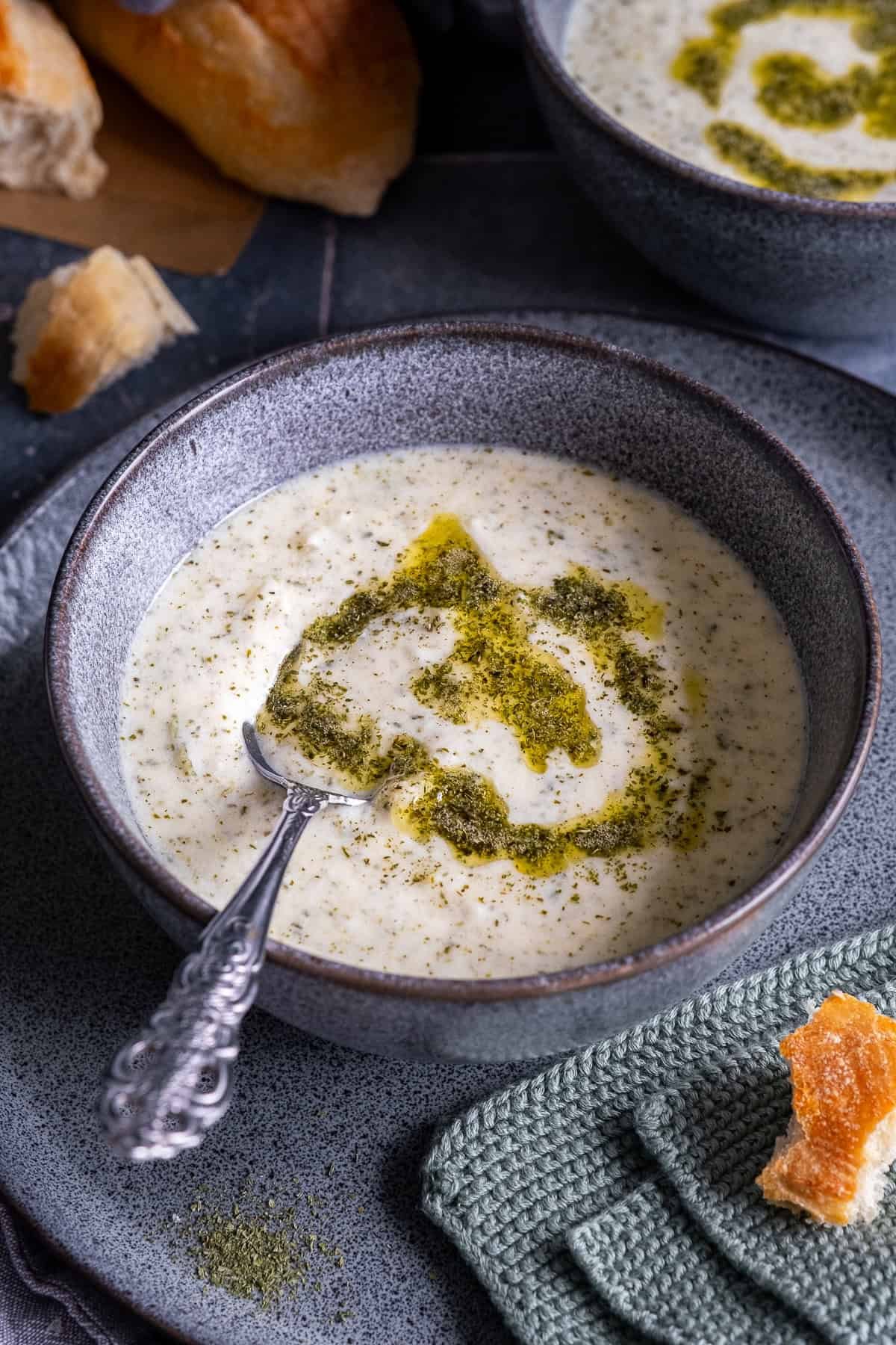 Close-up of a bowl of Turkish Yogurt Soup (Yayla Çorbası) topped with butter-mint sauce, served with bread on the side.