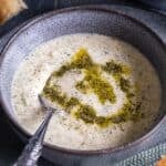 Close-up of a bowl of Turkish Yogurt Soup (Yayla Çorbası) topped with butter-mint sauce, served with bread on the side.