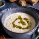 A bowl of Turkish Yogurt Soup (Yayla Çorbası) topped with butter-mint sauce, served with crusty bread in the background.