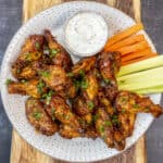 Buffalo wings with hot sauce served with carrot and celery sticks and a bowl of ranch dressing on a plate.