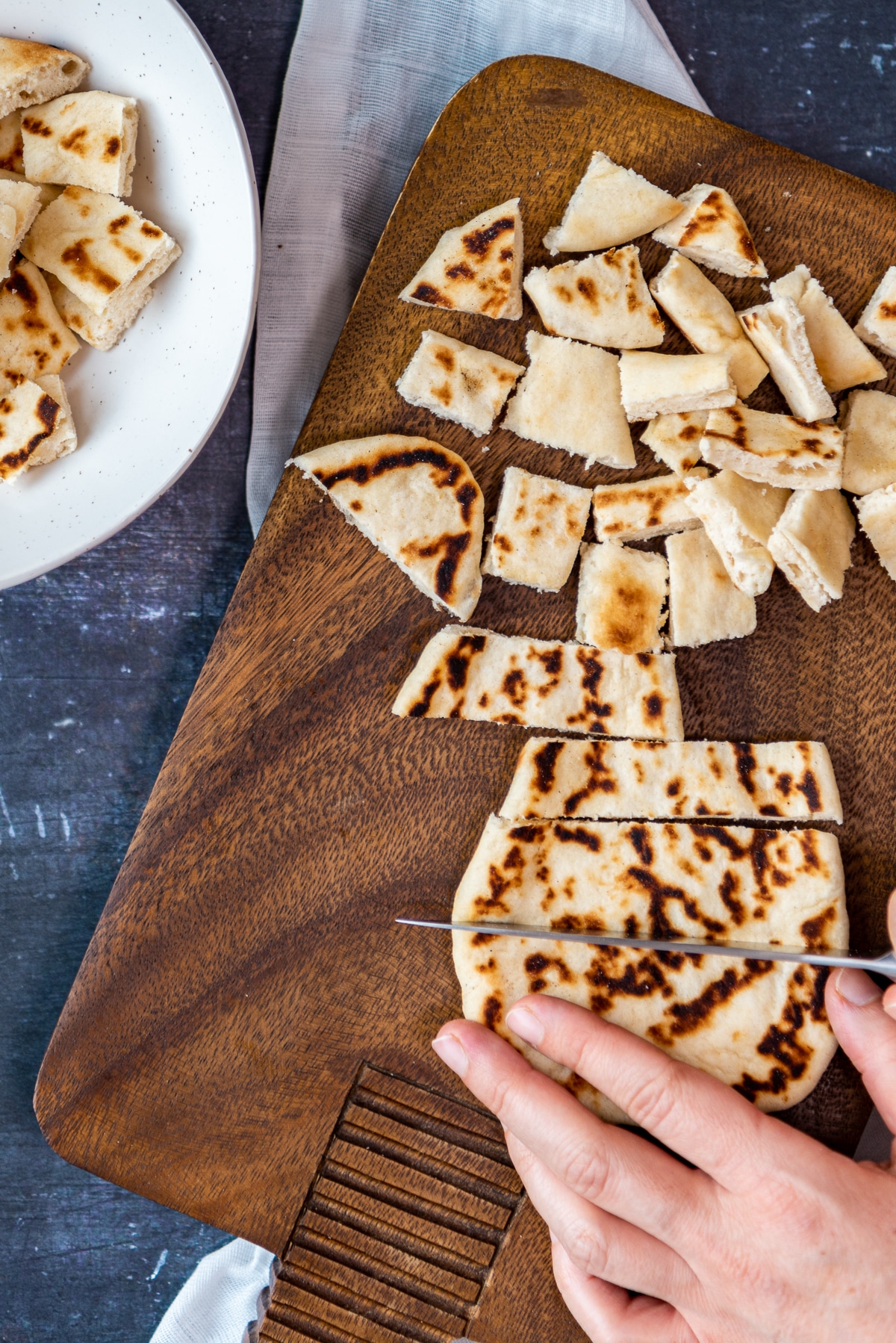 Hands cutting pide bread into chunks on a wooden board.