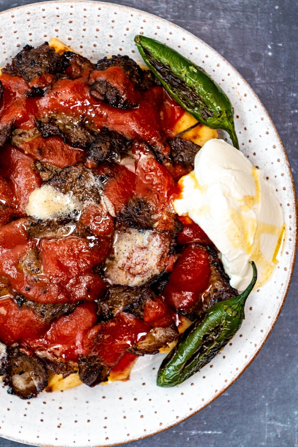 Homemade Iskender kebab served with tomato sauce, green peppers and yogurt on a plate.