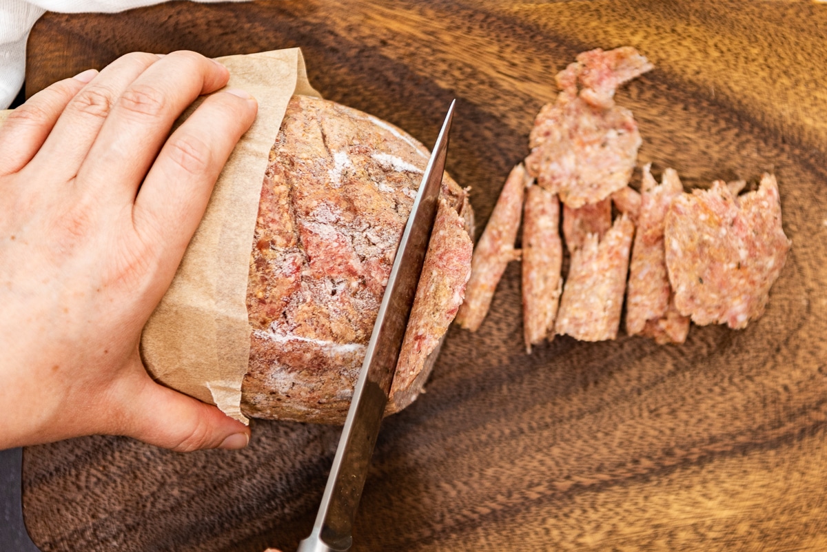 Hands slicing frozen ground beef log.