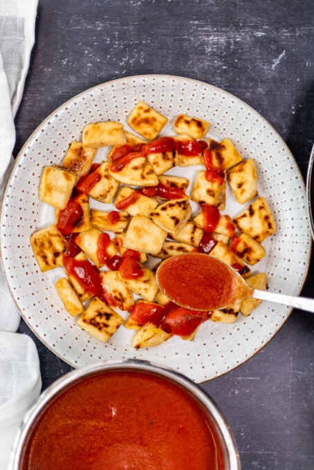 Pouring tomato sauce over pide chunks on a white plate.