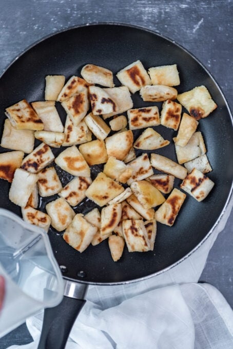 Pouring water over pide bread in a pan.