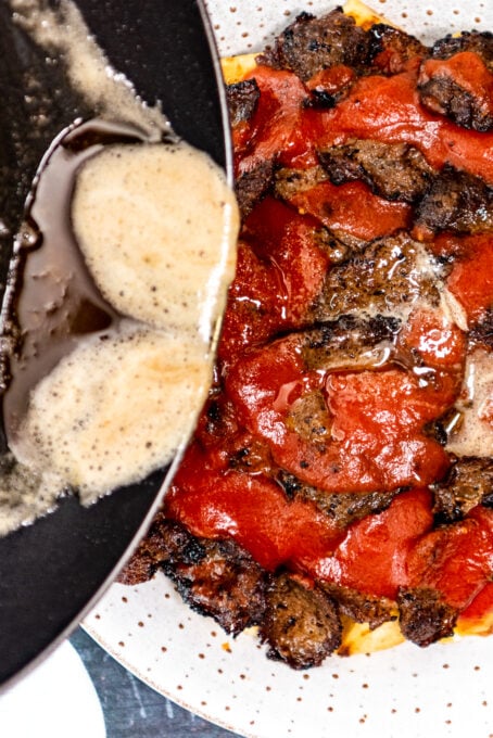 Pouring browned butter from a pan over iskender plate.
