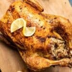 Roasted whole chicken stuffed with seasoned rice on a wooden board with lemon slices.