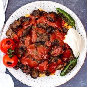Turkish iskender kebab served over toasted bread with sliced beef, rich tomato sauce, melted butter, yogurt, grilled green peppers, and roasted tomatoes.