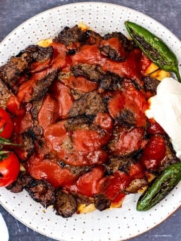 Turkish iskender kebab served over toasted bread with sliced beef, rich tomato sauce, melted butter, yogurt, grilled green peppers, and roasted tomatoes.