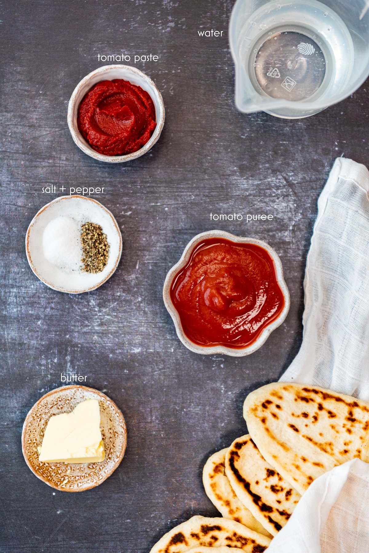 Tomato paste, passata, butter, spices and pide bread on dark background.