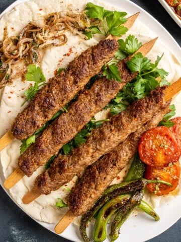 Adana kebab skewers on lavash with parsley, roasted tomatoes and green peppers.