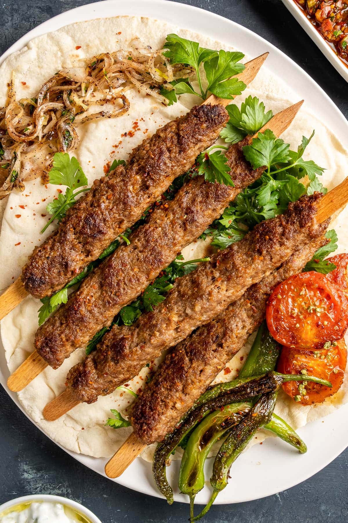 Adana kebab skewers on lavash with parsley, roasted tomatoes and green peppers.