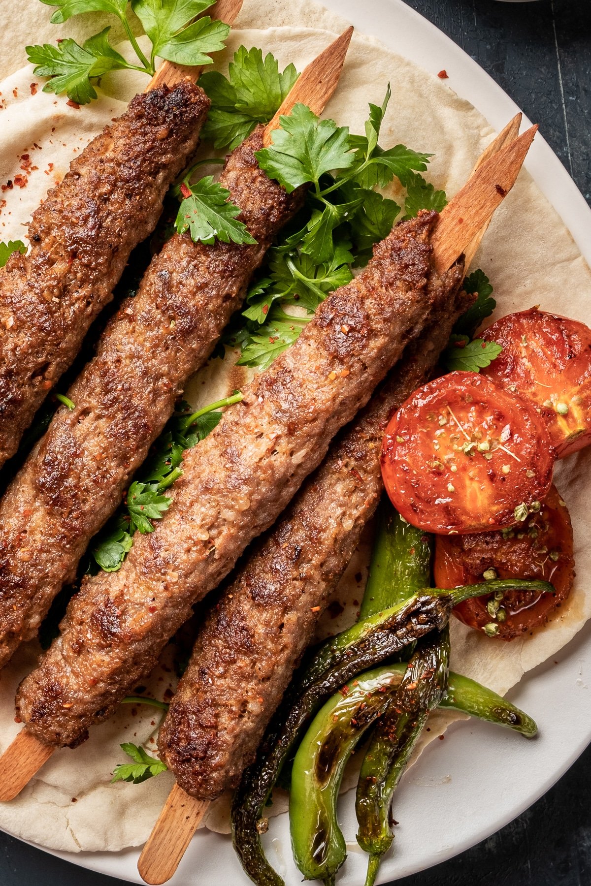 Homemade Adana lamb kebabs on lavash bread with parsley, tomatoes and green peppers.