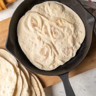 Lavash breads in an iron skillet on a wooden board and more lavash breads on the side.
