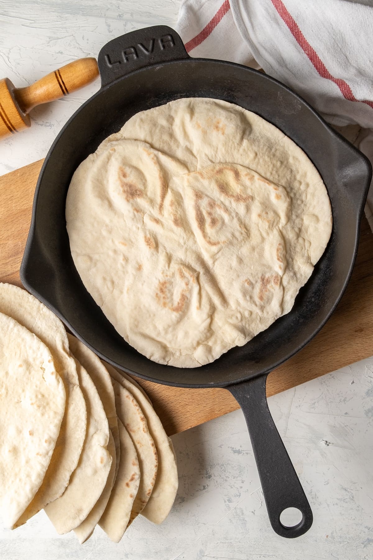 Lavash breads in an iron skillet on a wooden board and more lavash breads on the side.