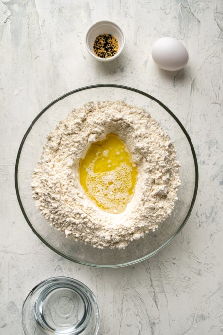 Flour, milk and olive oil in a large glass mixing bowl and water, sesame seeds and egg on the side.