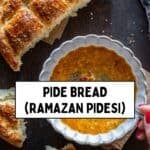 A bowl of Turkish soup garnished with spices, served with freshly baked Turkish Pide Bread. A person is holding a torn piece of bread, ready to dip.
