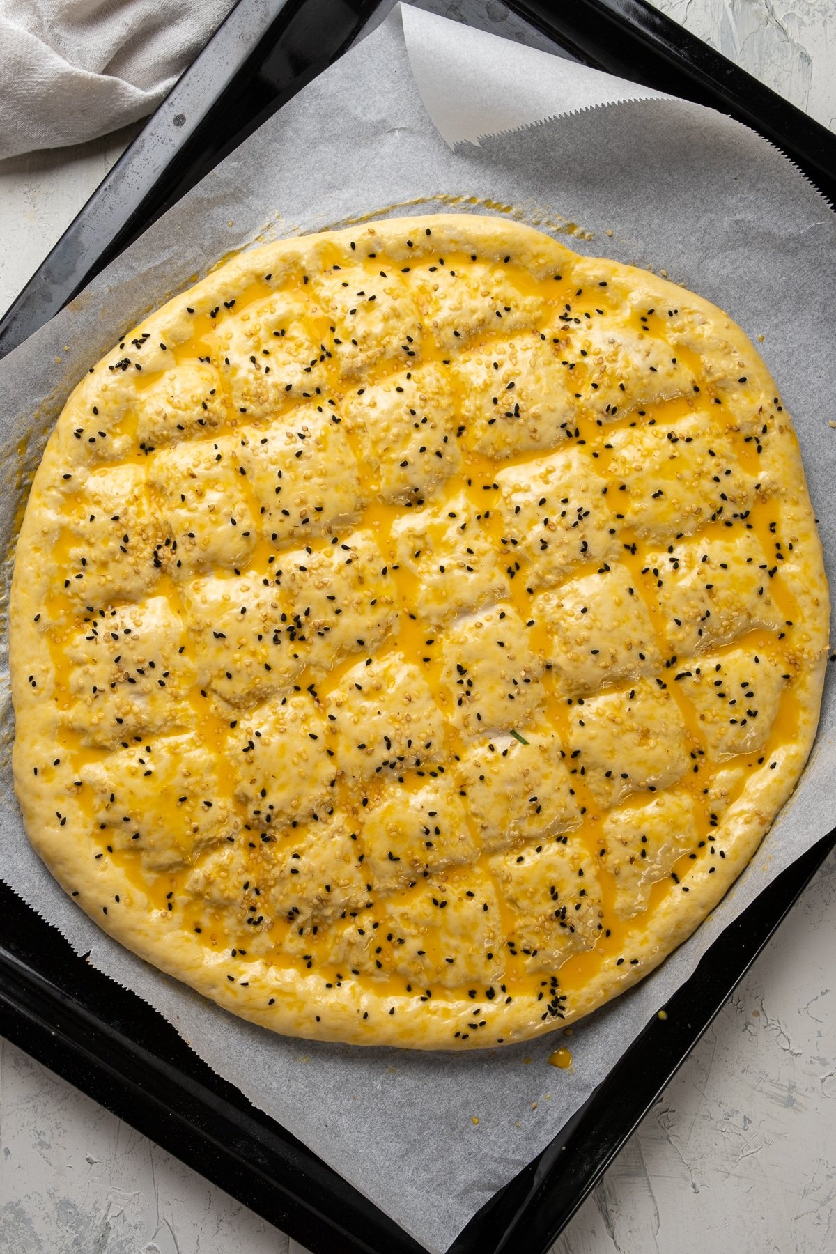 Ramadan bread dough with egg wash and sesame seeds on the top on a baking sheet.