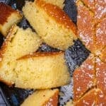 Overhead view of revani (Turkish semolina cake) cut into slices in a round pan, golden and syrup-soaked, topped with desiccated coconut.
