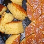 Overhead view of revani (Turkish semolina cake) cut into slices in a round pan, golden and syrup-soaked, topped with desiccated coconut.
