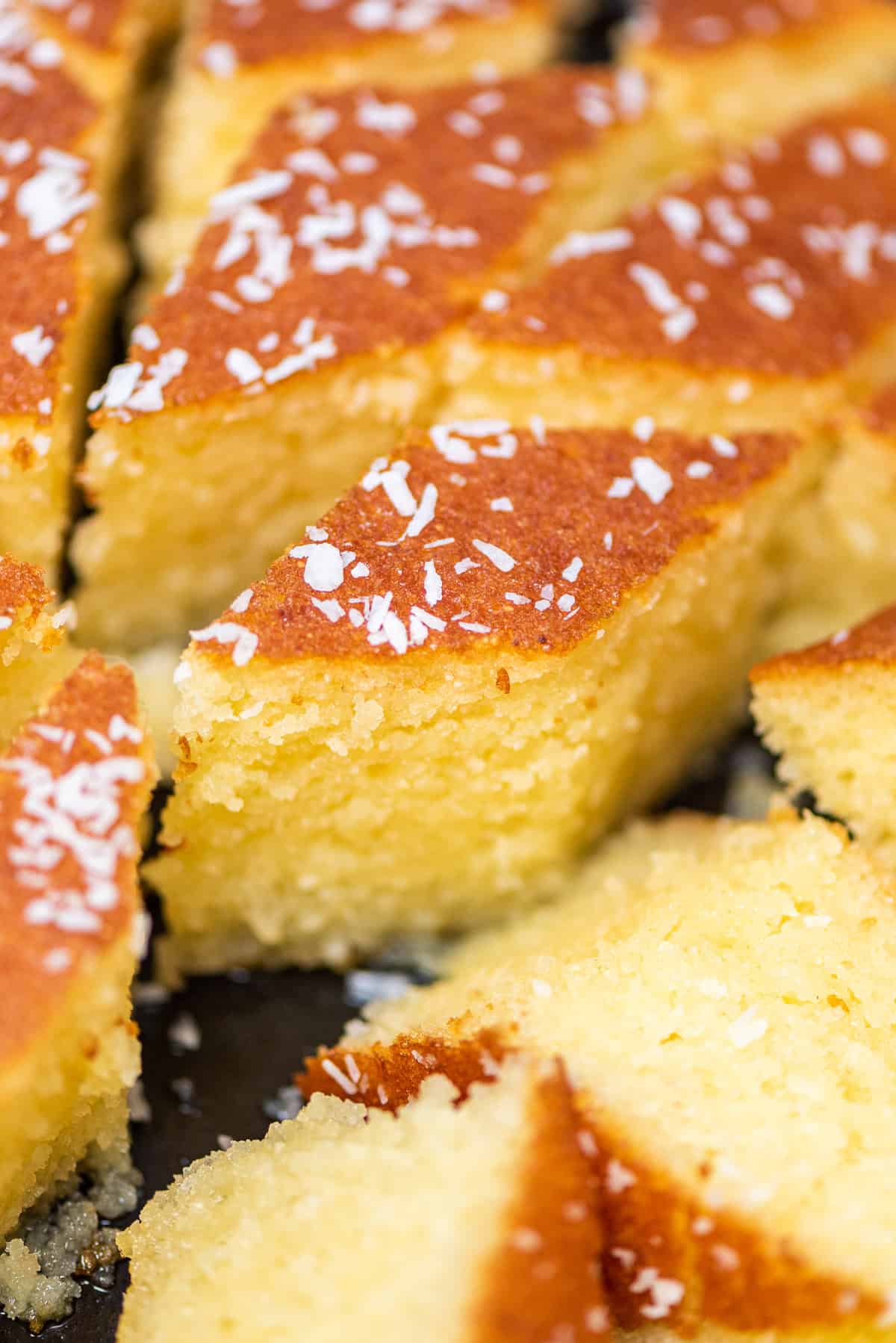 Close-up of revani (Turkish semolina cake) slices, golden and syrup-soaked with a soft crumb, topped with desiccated coconut.