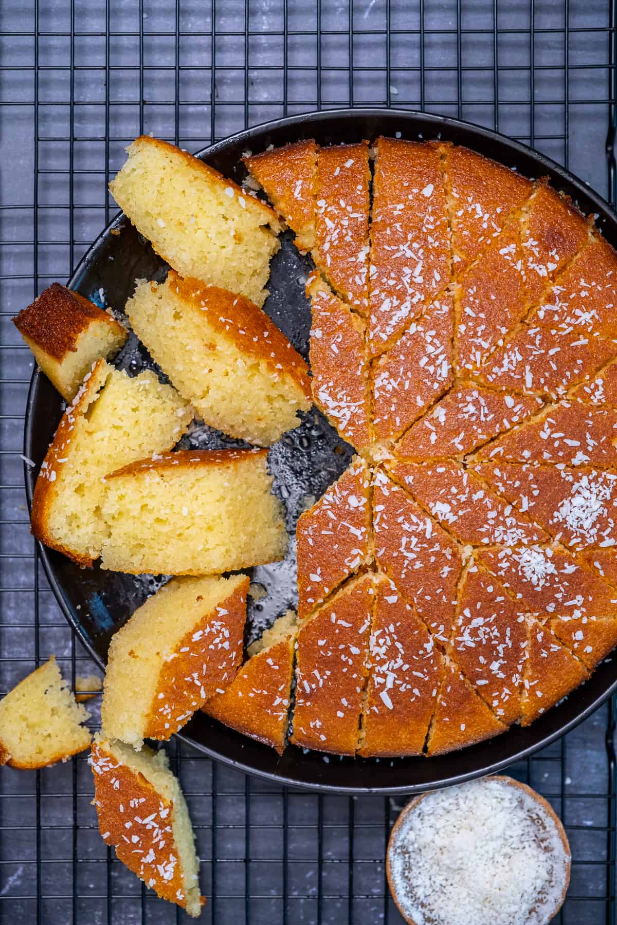 Revani sliced and garnished with coconut flakes on a black plate.