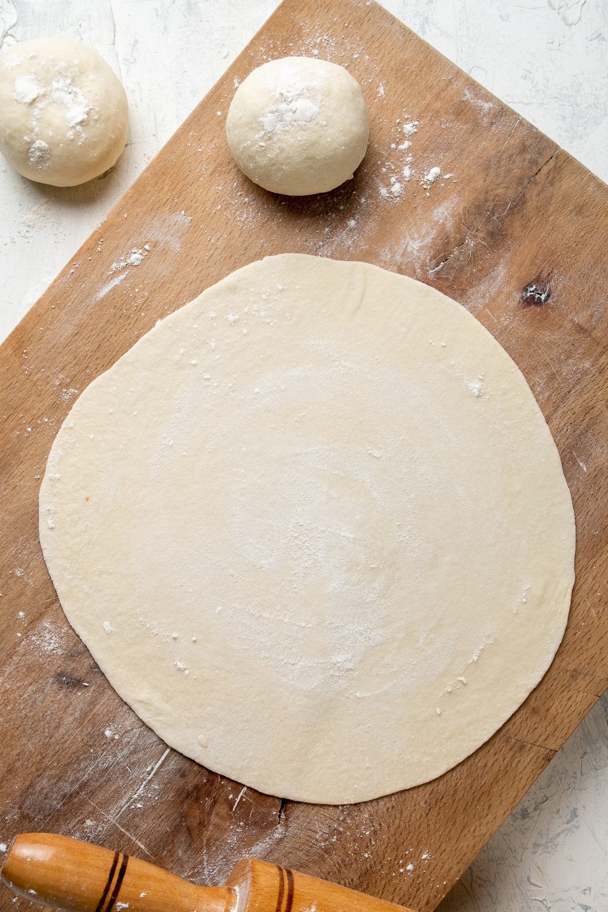 Rolled out dough on a wooden board and two dough balls on the side.