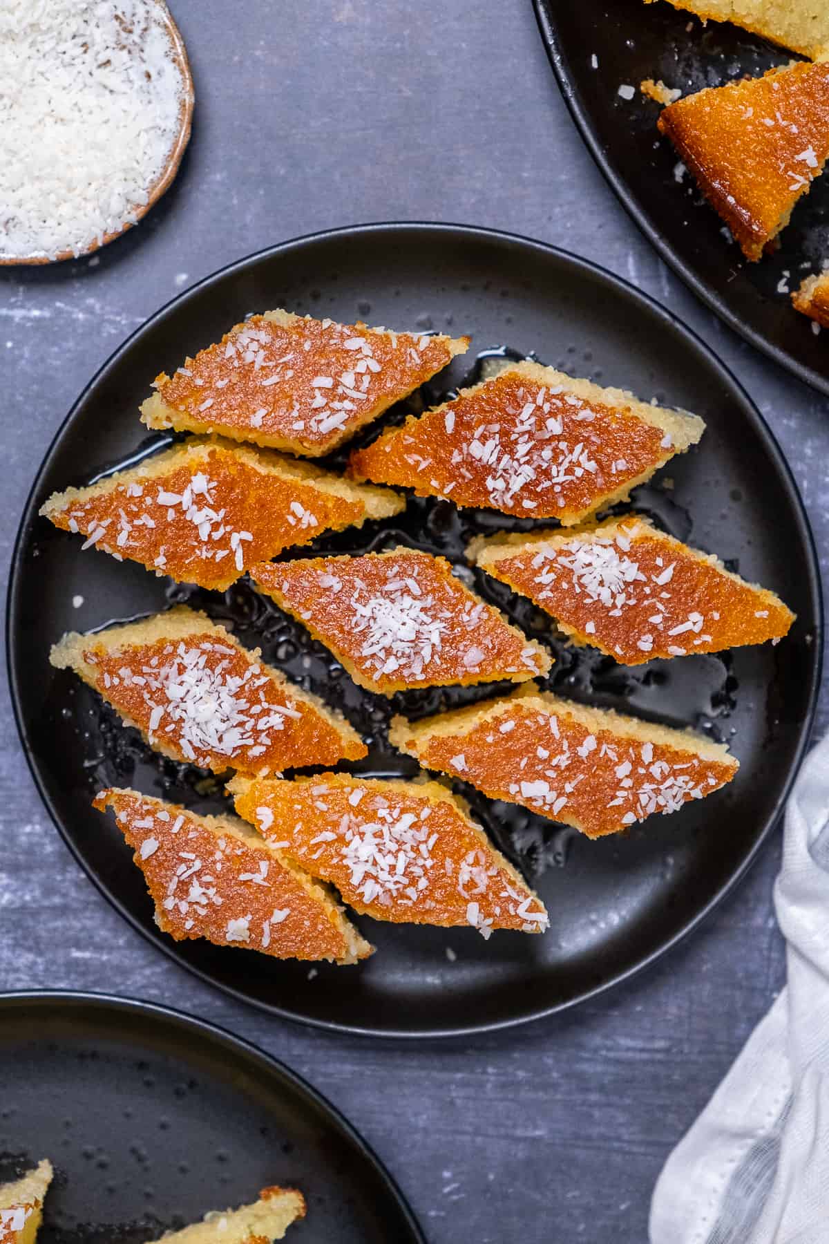 Semolina cake slices garnished with coconut flakes on a black plate.
