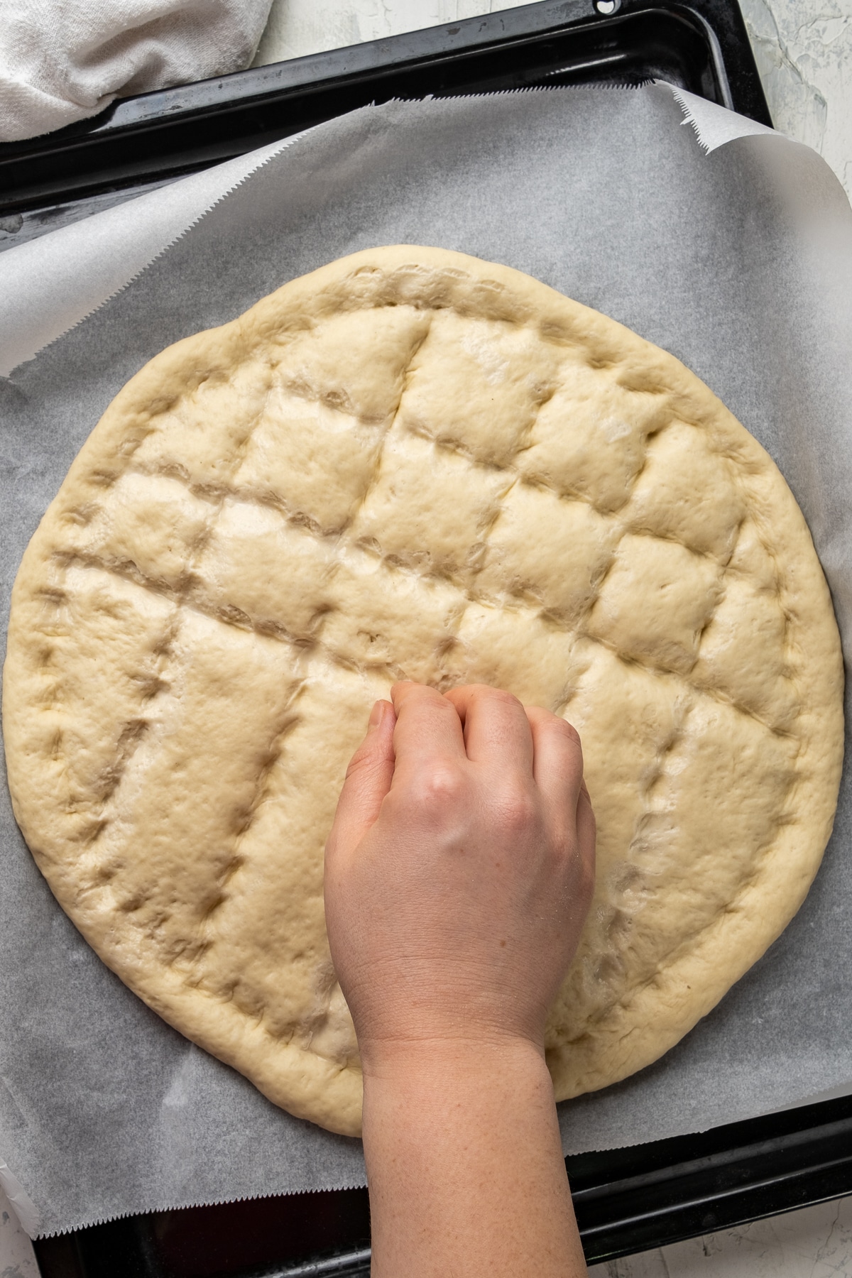 A hand shaping pide bread dough on a baking sheet with finger tips.