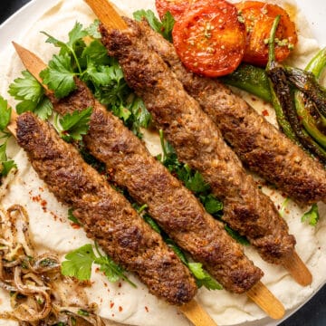 Adana kebabs served with roasted tomatoes and peppers, parsley and sumac onions on a lavash bread.