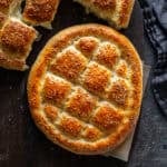 Golden Turkish Pide Bread with sesame seeds and a traditional diamond pattern, placed on a dark wooden surface. Another torn bread is visible in the background.