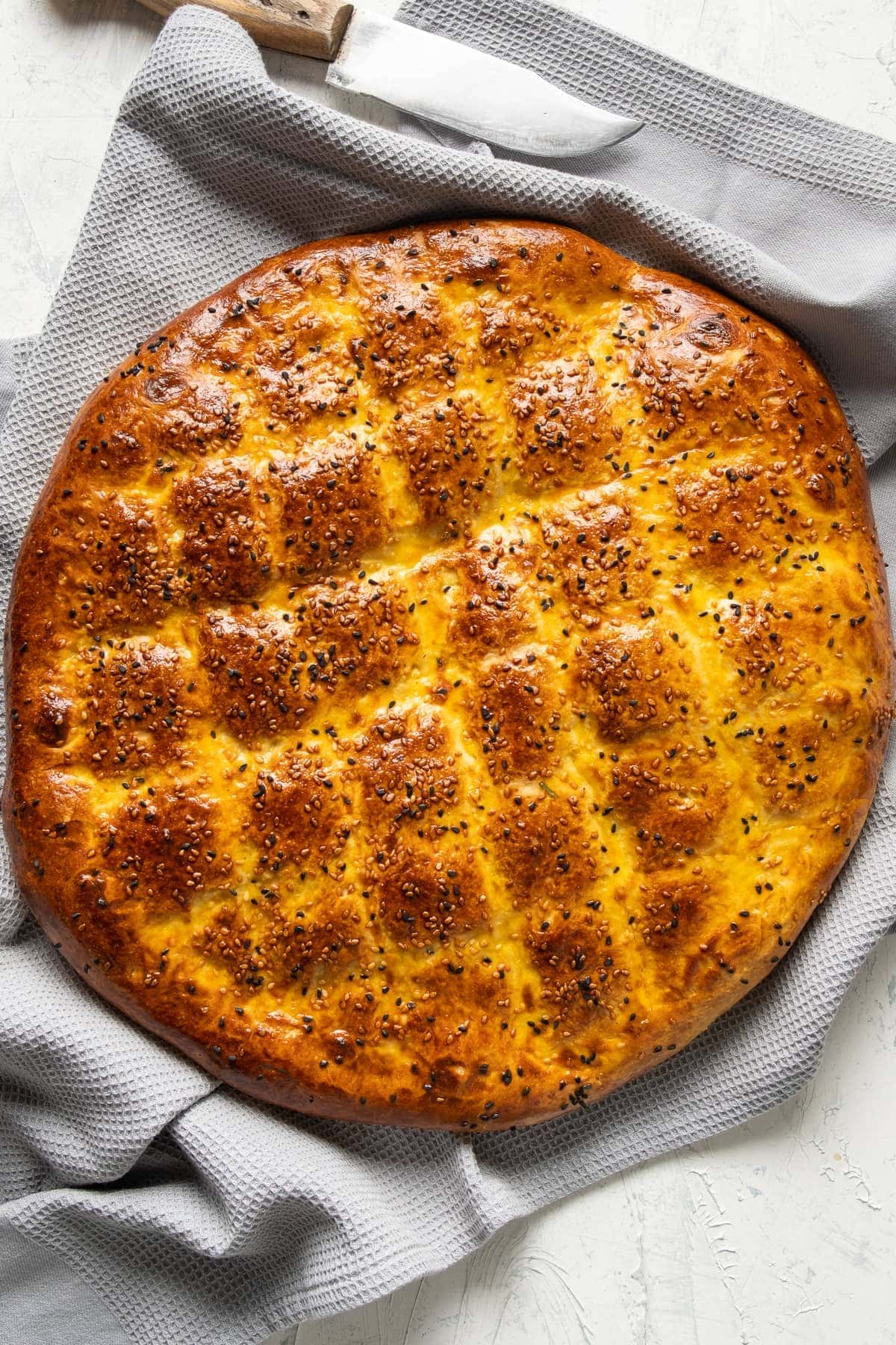 Newly baked pide bread with sesame seeds on a grey kitchen towel.