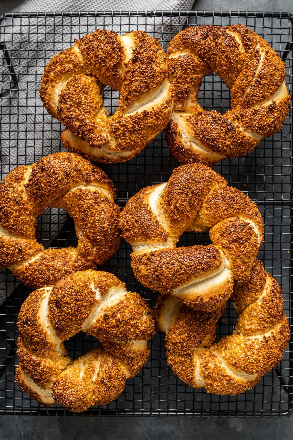 Turkish style bagels coated with sesame seeds called simit on a wire rack on a dark background.