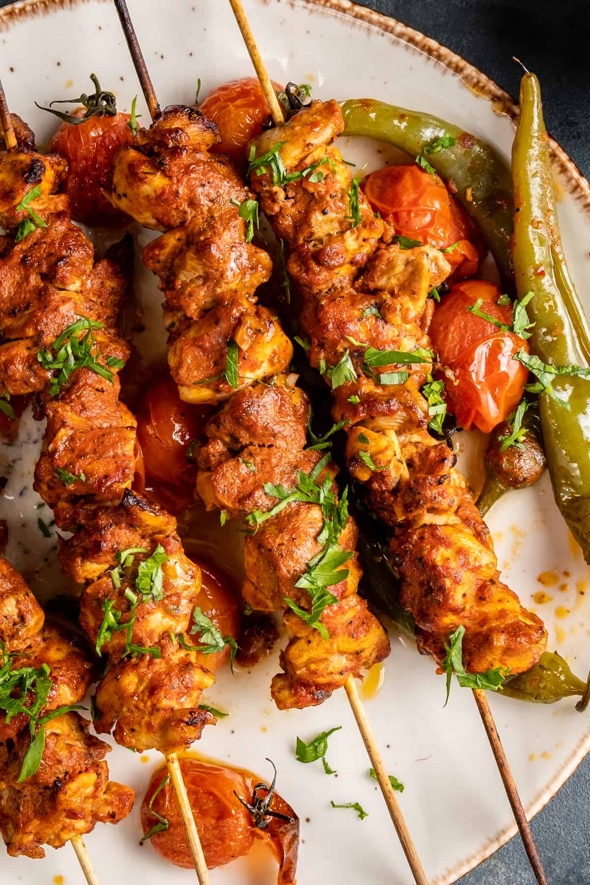 Chicken kebabs served with roasted tomatoes and green peppers on a white plate.