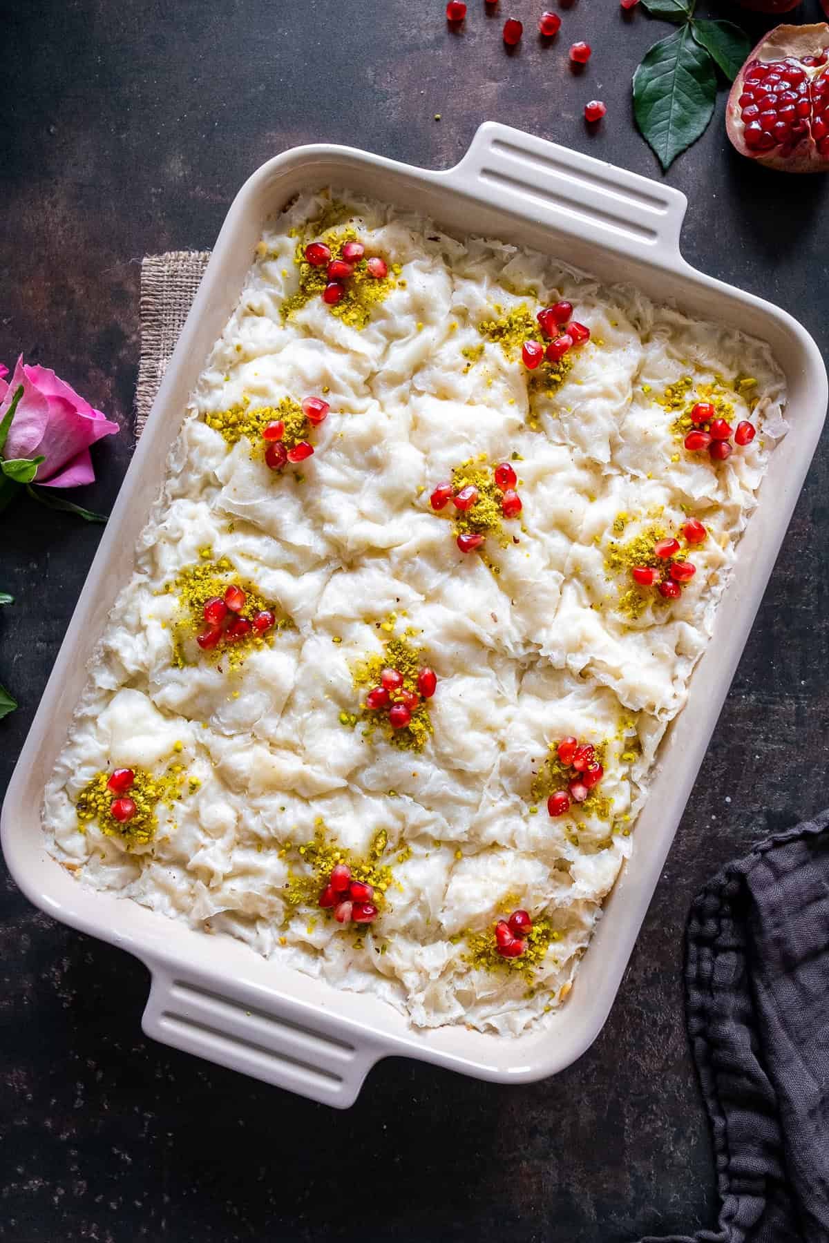 A tray of traditional Turkish Güllaç dessert, made with layers of thin starch wafers soaked in sweetened milk, garnished with ground pistachios and pomegranate seeds.