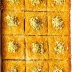 Overhead view of baked Turkish kadayıf dessert cut into square pieces in a tray, topped with chopped pistachios.