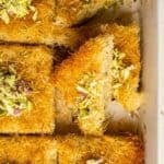 Close-up of Turkish kadayıf dessert with a piece being lifted, showing its crispy shredded layers and soft interior, topped with chopped pistachios.